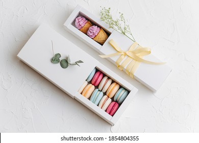 Sweets in rectangle pull out boxes. Colorful macarons and waffle cones with zefir on top. On a white surface. Arranged and decorated for composition.