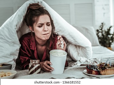 A Lot Of Sweets. A Stressed Woman Covered With A Blanket Eating A Lot Of Sweets