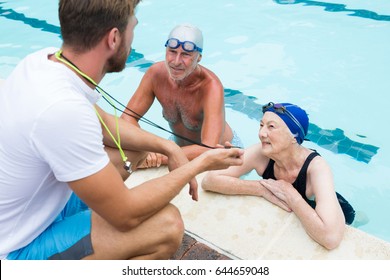 Swim coach showing stop watch to senior couple at poolside - Powered by Shutterstock