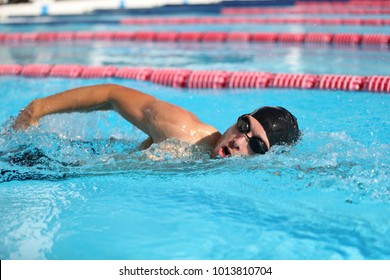 Swim Competition Swimmer Athlete Doing Crawl Stroke In Swimming Pool. Sports Man Male Swimmer With Goggles And Cap Breathing Racing In Indoor Stadium. Speed Exercise Workout.