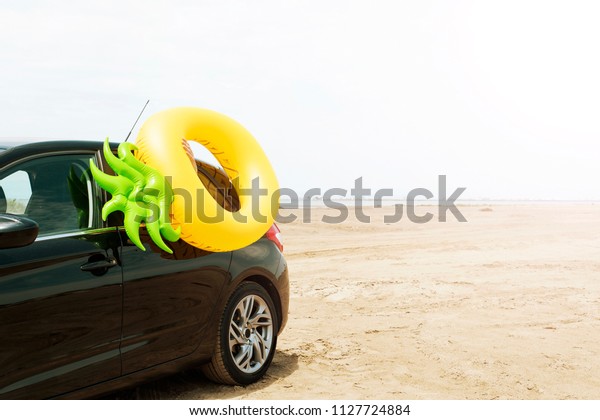 a swim ring in the shape of a pineapple on a car,\
on the sand of a beach, with the sea in the background, with some\
blank space on the right