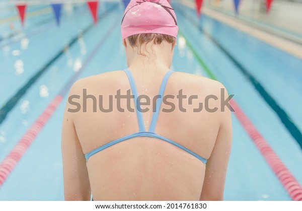Swimmer\
girl preparing for the start stands with her back to the camera on\
the background of the pool. Good quality\
photo.