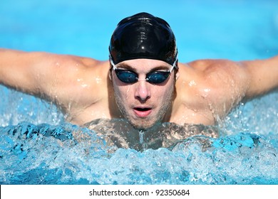 Swimmer. Man swimming butterfly strokes in competition. Competitive male sport swimmer wearing swimming goggles and cap. Young caucasian male fitness model.