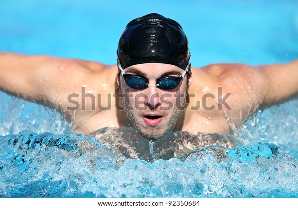 Swimmer. Man swimming butterfly\
strokes in competition. Competitive male sport swimmer wearing\
swimming goggles and cap. Young caucasian male fitness\
model.