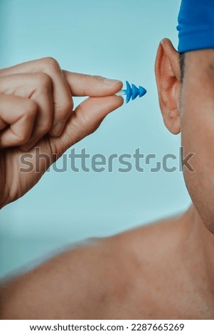 a swimmer man, wearing a blue swimming cap, puts an earplug in his ear, in a swimming pool
