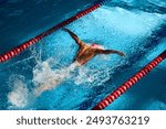 Swimmer in pink cap executes powerful butterfly stroke, his muscular form cutting through blue water, creating dynamic splash between red lane dividers. Concept of sport, preparation to competition