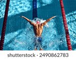 Swimmer, seen from above, powers through water with butterfly stroke, his muscular back glistening under sun as they swim between red lane dividers. Concept of aquatic sport, competition, energy.