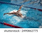 swimmer, sportsman performs powerful butterfly stroke, his muscular form creating dynamic splash as they glide through clear blue pool. Concept of aquatic sport, preparation to competition, energy.