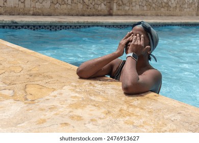 Swimmer taking a break, covering face with hands, wearing goggles and swim cap, at poolside. - Powered by Shutterstock