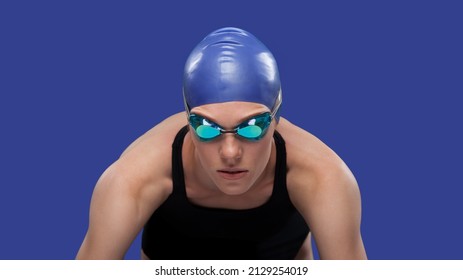 Swimmer woman on the start ready to jump to the pool. Studio portrait against solid blue background - Shutterstock ID 2129254019
