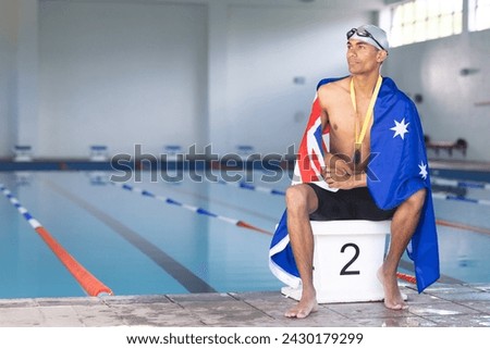 Swimmer wrapped in an Australian flag sits poolside with a medal, with copy space. The setting suggests a competitive atmosphere at an indoor swimming facility.
