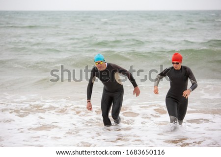Swimmers in wetsuits in sea waves. High angle view of athletic people in sportswear in water during competition. Triathlon concept
