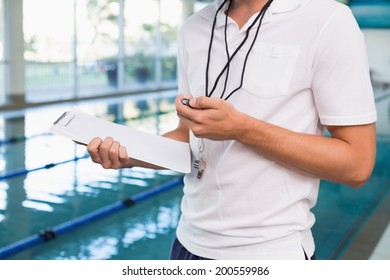 Swimming coach looking at his stopwatch by the pool at the leisure center - Powered by Shutterstock