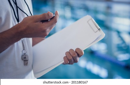 Swimming coach looking at his stopwatch by the pool at the leisure center - Powered by Shutterstock