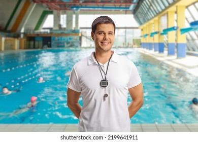 Swimming coach with a wistle and stopwatch posing inside an indoor swimming pool