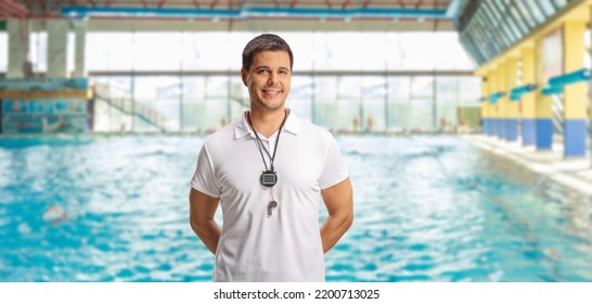 Swimming coach with a wistle and stopwatch posing on an indoor swimming pool - Powered by Shutterstock