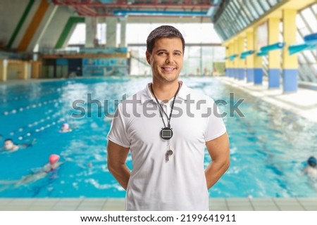 Swimming coach with a wistle and stopwatch posing inside an indoor swimming pool
