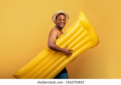 Swimming Is Fun. Joyful Black Man In Swimwear Going To Pool With Inflatable Lilo Over Yellow Studio Background. Cool African American Guy Having Beach Party, Enjoying Summertime Rest