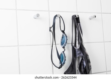 Swimming Goggles And Bathing Suit Hanging On Tile Wall