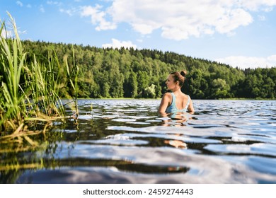 Swimming in lake in Finland. Woman in summer at beach. Finnish bathing in water in nature. Back view of person. Blue sky and beautiful green forest. Relax in Scandinavia after cottage sauna. - Powered by Shutterstock