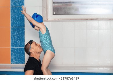 Swimming Lesson For A Girl In The Pool With A Coach, A Child In A Swimsuit, A Coach In A Wetsuit, A Man Raised The Girl High For A Jump And She Is Happy, She Has Fun