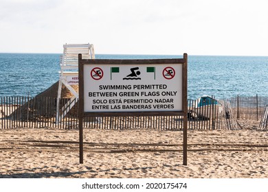 Swimming permitted between green flags only on a beach with a life guard stand and the long Islnad Sound in the background.
