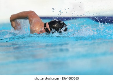 Swimming pool athlete training indoors for professional competition. Swimmer man on swim practice in stadium doing crawl with arm splashing water. Copy space on blue water background.