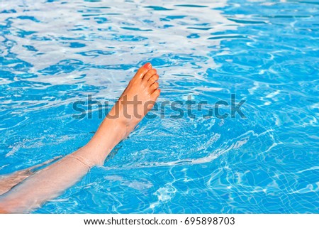 Swimming pool with blue tiles, outdoor pool with fresh water, swimming in the summer heat, clean water for swimming, leisure lifestyle, feet of the girl in the pool

