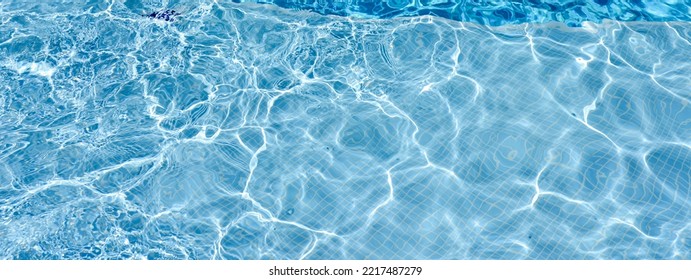 Swimming Pool With Blue Water, Ripples And Highlights. Texture Of Water Surface And Tiled Bottom. Overhead View. Summer Background.