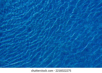 Swimming Pool With Blue Water, Ripples And Highlights. Texture Of Water Surface And Tiled Bottom. Overhead View. Summer Background.