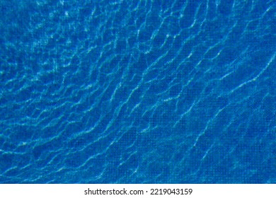 Swimming Pool With Blue Water, Ripples And Highlights. Texture Of Water Surface And Tiled Bottom. Overhead View. Summer Background.