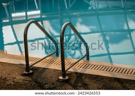 Swimming pool with clean clear water with reflection of palm and roof. Unfocused grab bars ladder. Focus on the water. Summer and travel concept. Abstract pool texture, underwater pattern