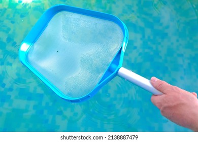 Swimming Pool Cleaning.Net for cleaning the pool in male hands on blue water background.Filtration of water with a net.Pool cleaning tool.