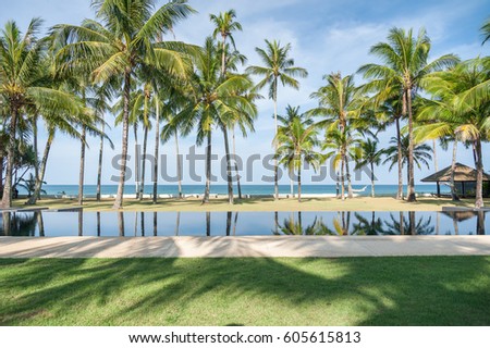 Swimming pool with coconut tree and sea background, reflection of coconut trees and white cloud and blue sky on the swimming pool at the beach
