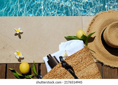 Swimming pool essentials concept. Beach bag with items for safe sunbathing on the deck, sunglasses, straw hat, white blanket and sunscreen product. Copy space, top view, background. - Powered by Shutterstock