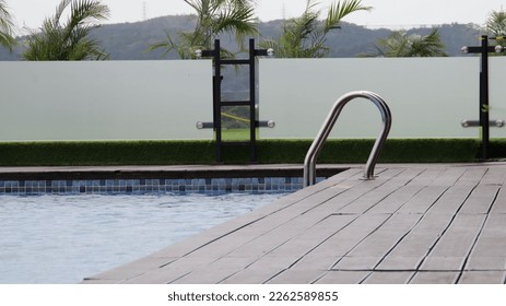 Swimming pool hand rail or stair ladder to help get in or get out of the pool. Beautiful edge of the swimming pool with a wooden deck. - Powered by Shutterstock