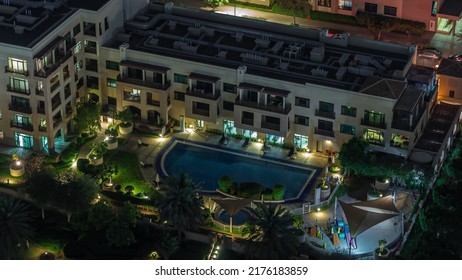 Swimming Pool And Low Rise Illuminated Buildings In Greens District Aerial Night Timelapse. Dubai Skyline With Palms And Trees