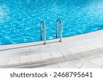 Swimming pool with stair and water. Swimming pool with handrail. Stainless steel ladder in pool. Grab bars ladder in the blue swimming pool