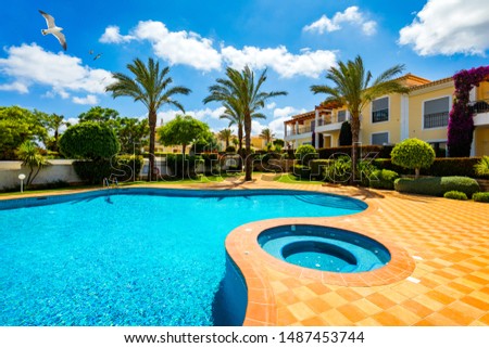 Swimming pool, sun-loungers and palm trees during a warm sunny day, paradise destination for vacations. Backyard swimming pool with garden full of palm trees and flowers. Backyard with swimming pool.