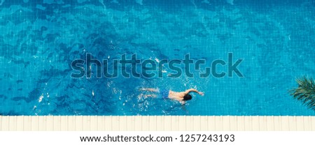 Swimming pool top view angle which young man relaxing and enjoying in pools of his hotel in summer season of Thailand at vacation day and have sun light and flares on blue water surface.