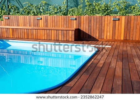 Swimming pool with wood deck and wood cladding fence and seat bench, backyard poolside decking design