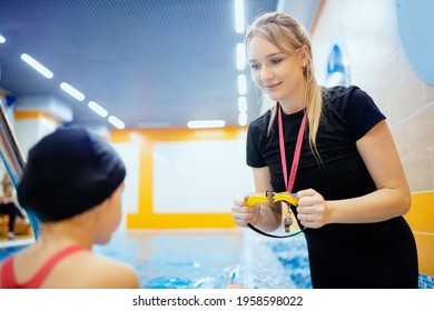 Swimming training school for children, woman trainer helps to put on glasses for kid girl, preparation for lesson. - Powered by Shutterstock