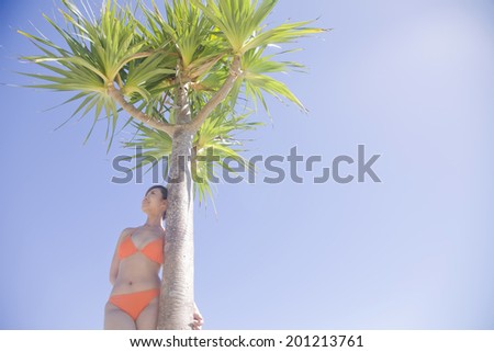 The swimsuit woman smiles while leaning against the palm trees