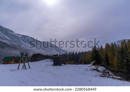 Swing against the backdrop of a holiday home near the forest on the snow under the mountain with fog and white snow, with the light of the moon on a bright night in the Altai in Siberia.
