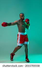 Swing Blow. Young Professional Male Boxer Practicing Punches On Blue Green Background In Neon Light. Full Length. Health, Sport And Motion Concept. Copy Space For Ad.