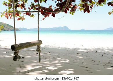 Swing Made From Natural Rope And Wood Log On White Sand Beach Under Giant Tree With Crystal Clear Bright Blue Sea Water In Background. Travelling On Vacation And Holiday To Tropical Island.