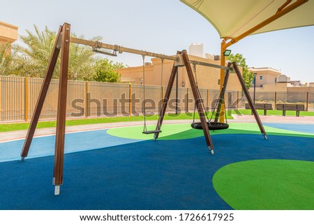 Swings in Dubai's public park, regular and nest type, above the rubber floor covered with the tensile shade canopy, summertime
