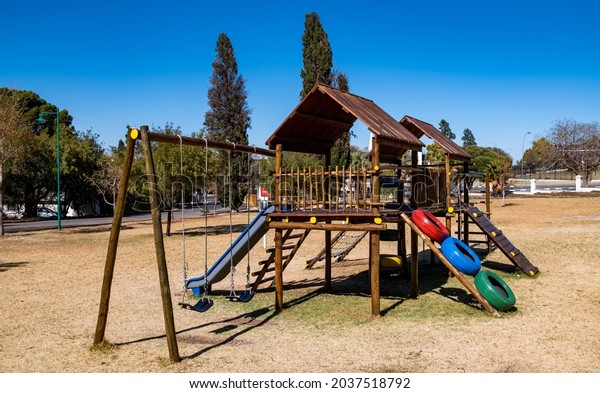 Swings and a jungle gym on a playground for\
younger children.  Wooden\
construction.