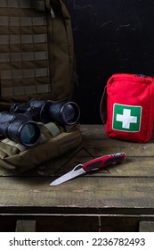 Swiss army knife and first aid kit. Binoculars and military backpack on a military box. Vertical frame. - Shutterstock ID 2236782493