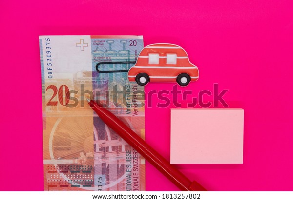 Swiss banknote, toy car paper clip, pen and\
stickers on pink\
background